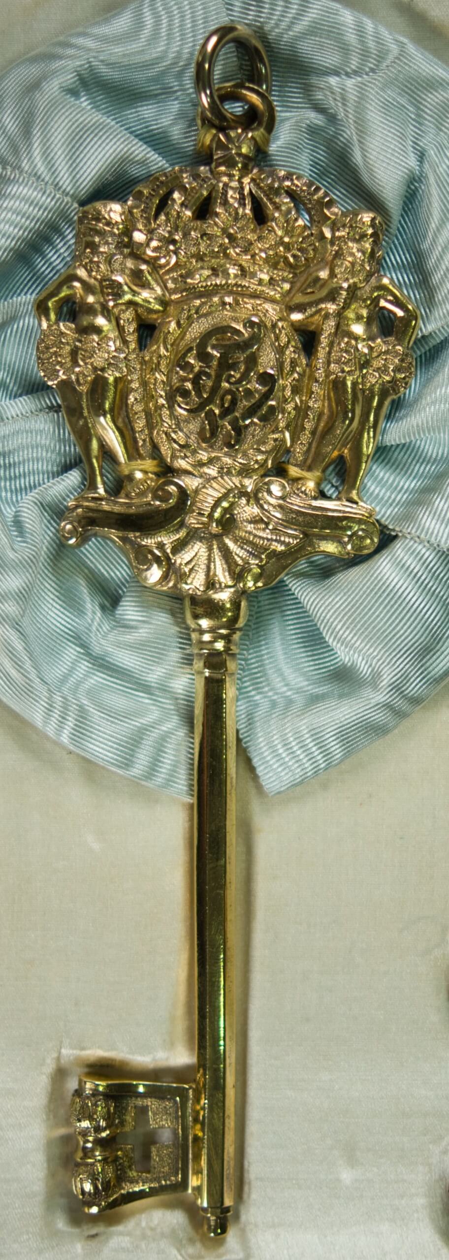 Ein preußischer Kammerherrenschlüssel (um 1910) mit blauer Seidenrosette und Befestigungsbändern in einem geöffneten Etui.