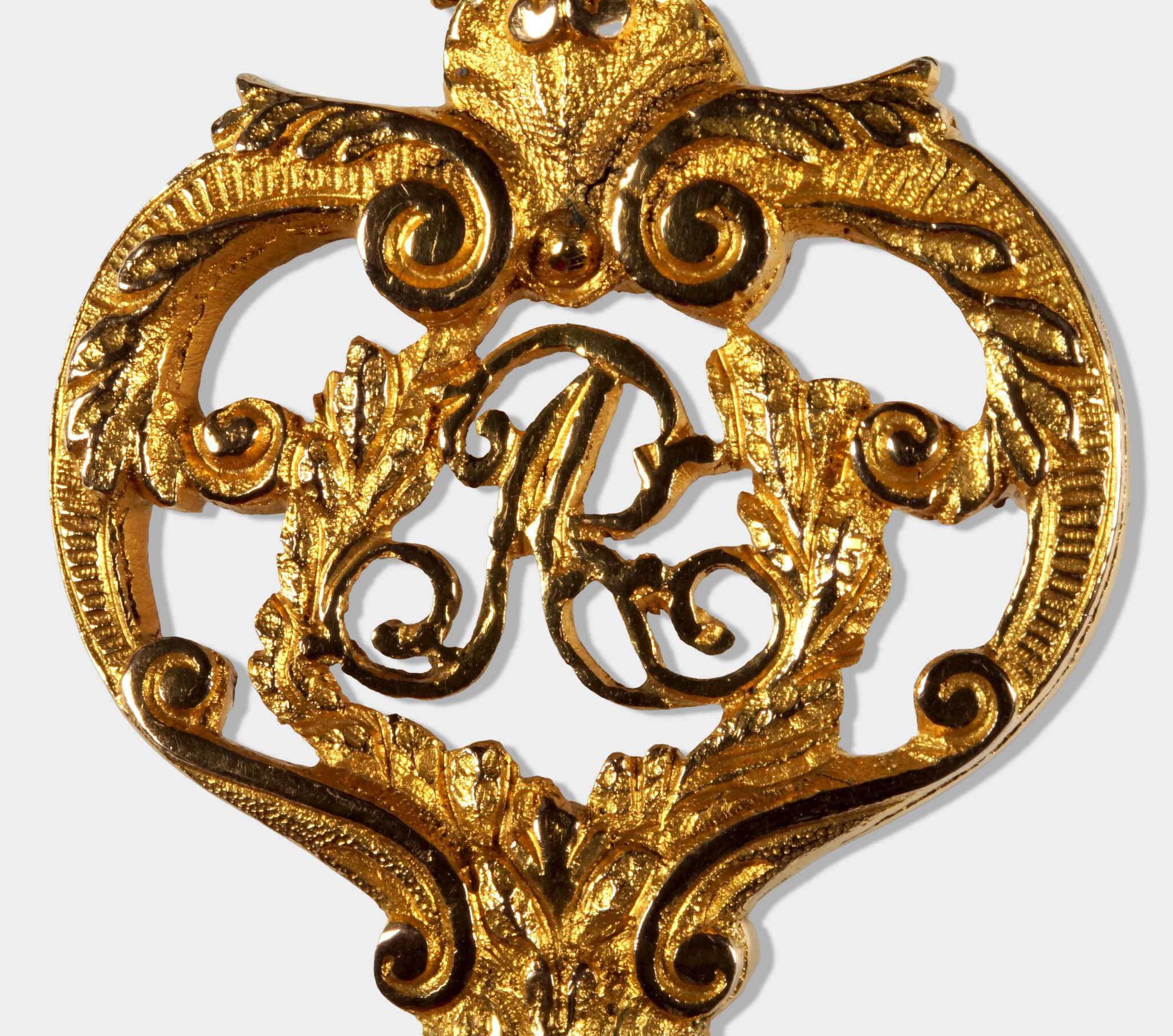 Nahaufnahme des Zentrums der Reide eines sächsischen Kammerherrenschlüssels mit dem Monogramm AR unter der Krone, flankiert von Voluten und Blätterranken.